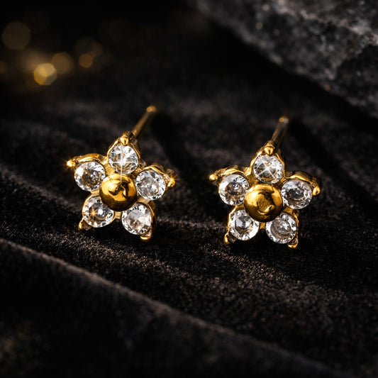 Gold flower-shaped earrings with clear gemstones on a black textured surface