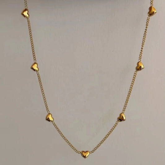 A gold chain necklace featuring multiple small, polished heart-shaped charms spaced along the chain, displayed against a plain light gray background.